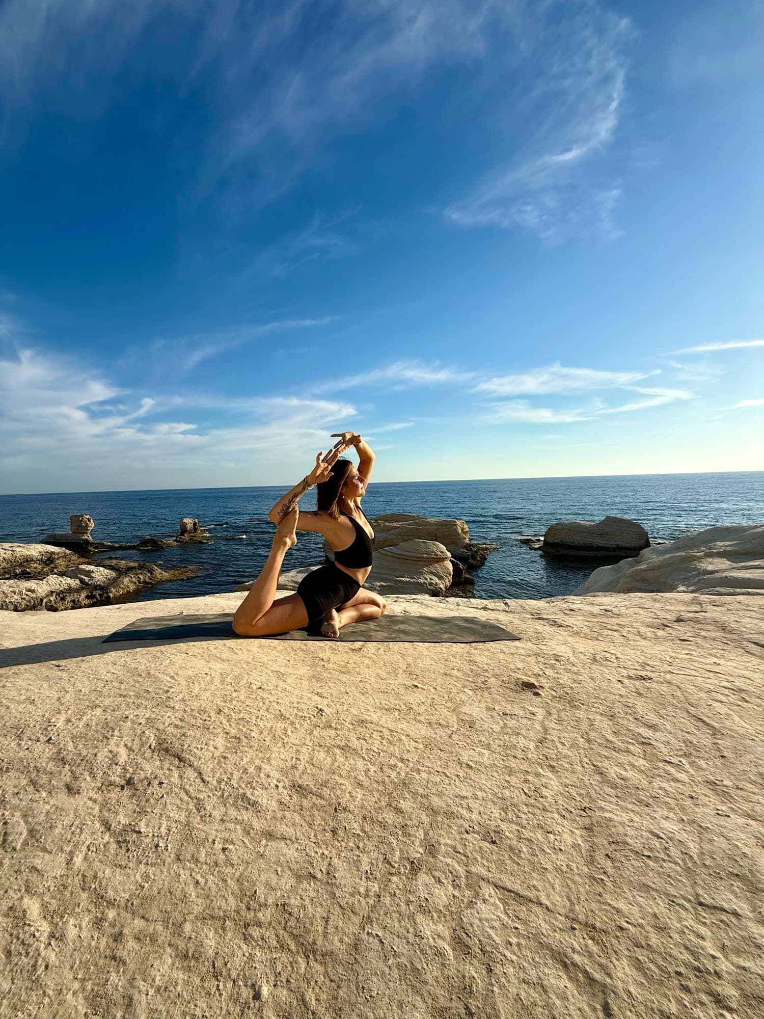 Laura in der Taubenpose auf hellen Felsen am Meer