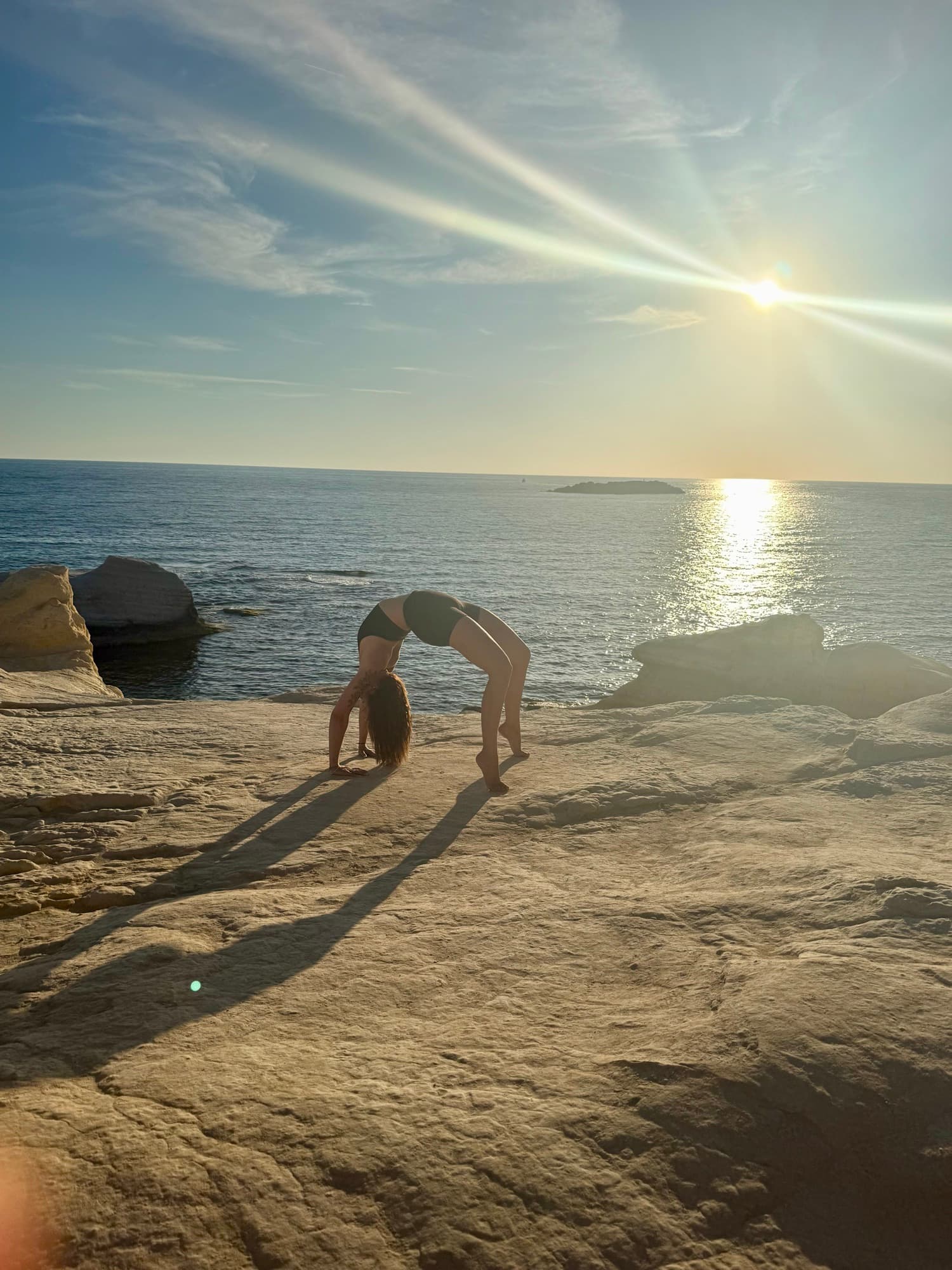 Laura in der Brücken-Pose auf Felsen am Meer bei Sonnenuntergang